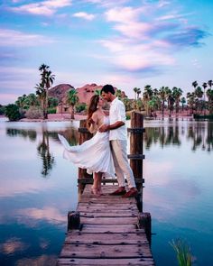 a bride and groom standing on a dock in front of the water with palm trees