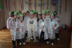 a group of children wearing lab coats and green hats posing for a photo in front of some streamers