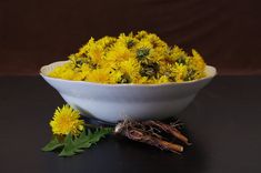 a white bowl filled with yellow flowers on top of a black table next to some roots