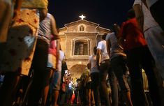 a group of people standing in front of a church at night with the lights on