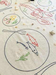 an embroidered tablecloth with fish and sea creatures on it, surrounded by seashells