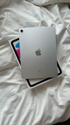 an apple ipad sitting on top of a white bed next to a black and pink sticker