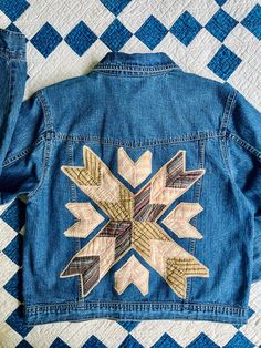 the back of a jean jacket with an embroidered snowflake design on it, sitting on top of a quilt