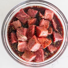 raw meat in a glass bowl with spices and seasoning on the side, ready to be cooked