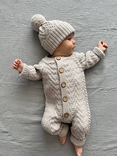 a baby wearing a knitted sweater and hat laying on a bed next to a blanket