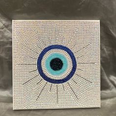 a blue and white square with an evil eye on the center, in front of a silver background