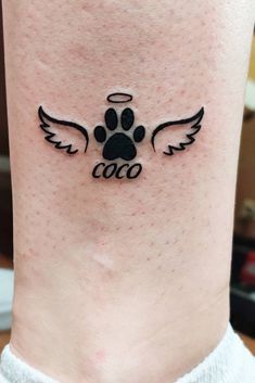 a dog's paw with an angel wing tattoo on the ankle, which reads cooo