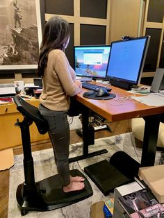 a woman sitting at a desk with a laptop and computer monitor on top of it