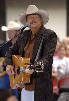 a man in a suit and hat holding a guitar while standing next to a microphone