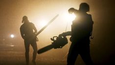 two people holding chainsaws in the dark with headlights behind them and foggy sky