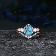 a turquoise and white stone ring sitting on top of a black rock in front of a dark background