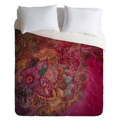 a bed covered in pink and purple comforter covers with flowers on it, along with two pillows