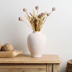 a white vase filled with dried flowers sitting on top of a wooden table next to other items