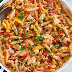 pasta with chicken, peppers and parsley in a white bowl on a black and white striped cloth