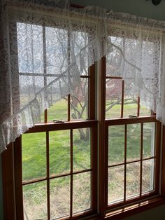 two windows with white lace curtains and green grass in the back ground, one window is open