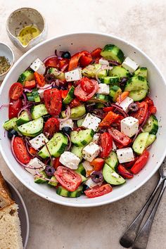 a white bowl filled with cucumbers, tomatoes and olives next to bread