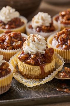 cupcakes topped with caramel and whipped cream on a metal tray next to other dessert items