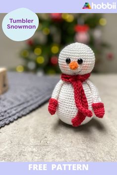 a knitted snowman sitting on top of a table next to a christmas tree