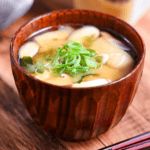 a wooden bowl filled with soup next to chopsticks on top of a table