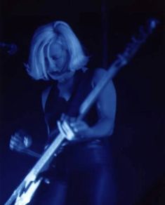 a woman with blonde hair playing a guitar in front of a microphone and some lights