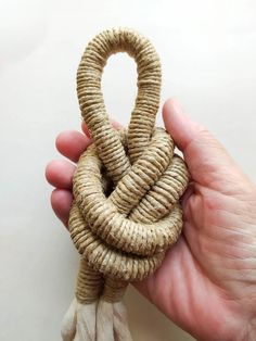 a hand holding a knot made out of jute and tasseled with rope