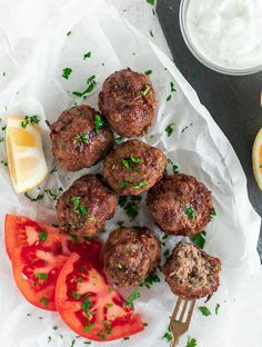 some meatballs and tomatoes are on a white plate with a fork next to it