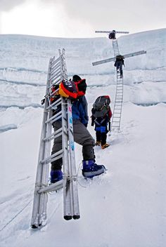 three people climbing up a ladder in the snow