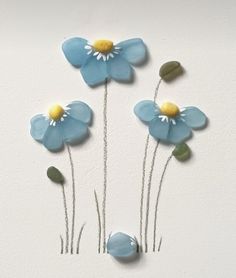 three blue flowers with yellow centers on a white wall