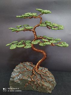 a wire bonsai tree on top of a rock with green beaded branches and leaves