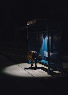 a person sitting on a bench in the dark with their feet up and head down