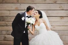 a bride and groom kissing in front of a wooden wall