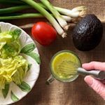 a person holding a knife over a plate with lettuce, tomatoes and avocado