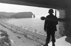 a man standing on the edge of a cliff looking out at water and cliffs in the distance