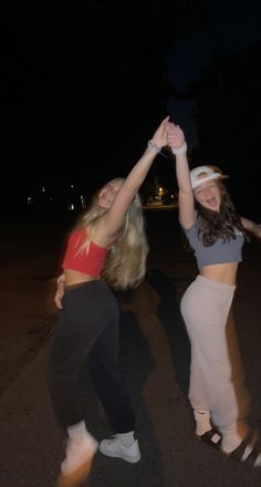 two young women are dancing on the street at night, one is holding her hand up