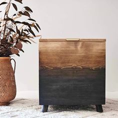 a wooden box sitting on top of a rug next to a vase filled with plants