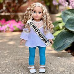 a doll is standing in the street with a sash around her neck and blue pants