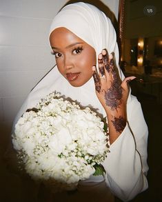 a woman holding a bouquet of flowers in front of her face with hendi tattoos