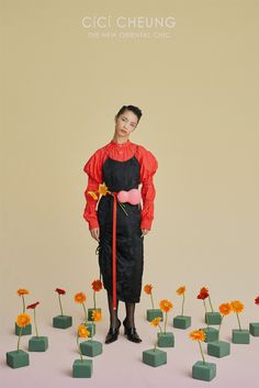 a woman standing in front of flowers with her hands on her hips and wearing an apron