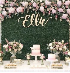 a table topped with cakes and desserts next to a wall covered in greenery