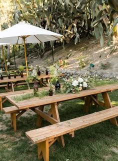 an outdoor picnic area with wooden benches and tables covered by umbrellas in the grass