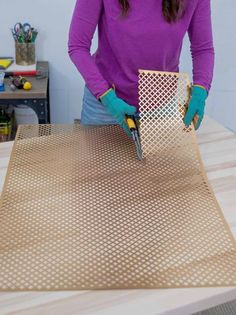 a woman in purple shirt and blue gloves working on a piece of metal mesh with scissors