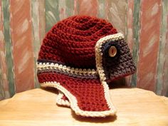 a crocheted red hat sitting on top of a wooden table next to a striped wall