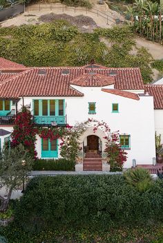 an aerial view of a white house with green shutters and red tile roofing