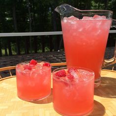 two glasses filled with raspberry lemonade sit on a table next to a pitcher