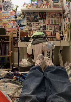 the person is laying down with their feet up in front of his desk and bookshelf