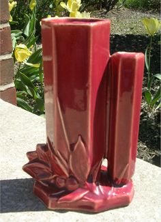 a red vase sitting on top of a cement slab