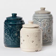 three ceramic canisters with designs on them are lined up against a white background