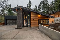 a modern home in the woods with wood siding and stone accents on the front door