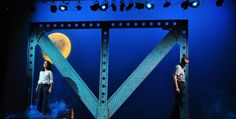 two men standing on stage in front of a blue background with the moon behind them