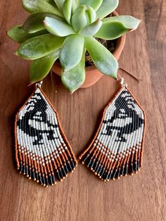 a pair of beaded earrings sitting on top of a wooden table next to a potted plant